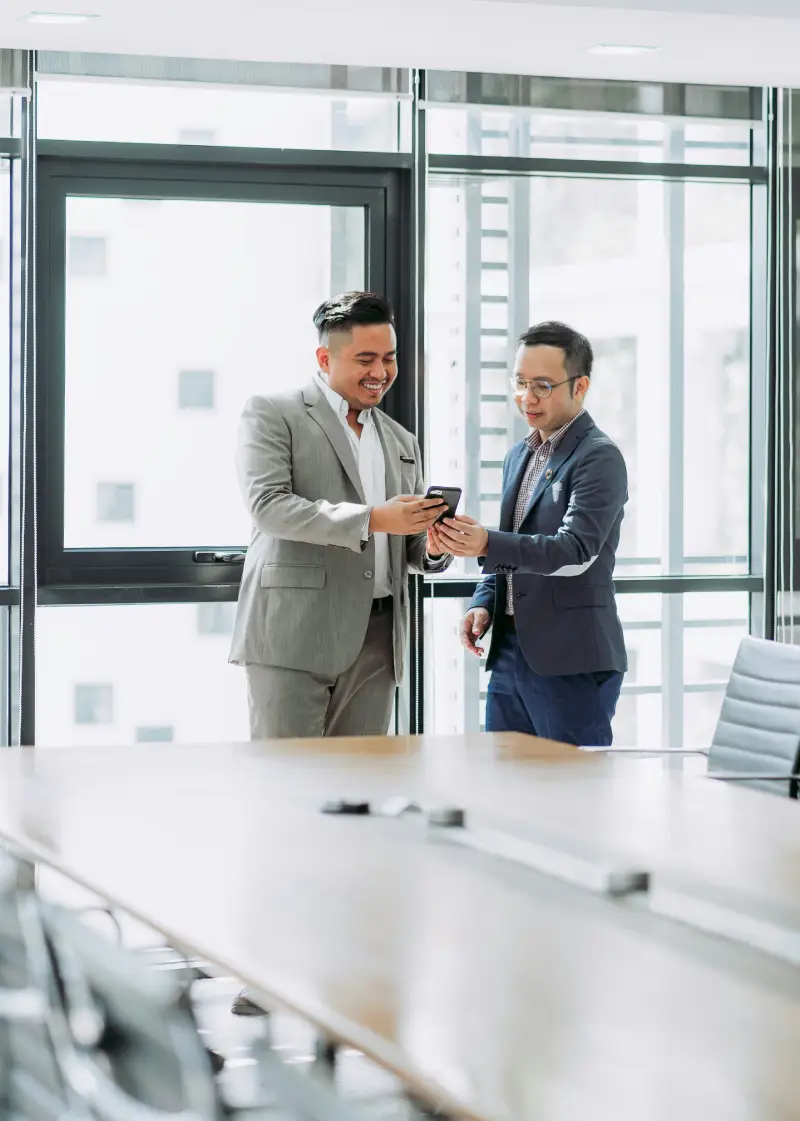 Two business professionals are engaged in discussion while examining a mobile device in a modern conference room Two business professionals are engaged in discussion while examining a mobile device in a modern conference room